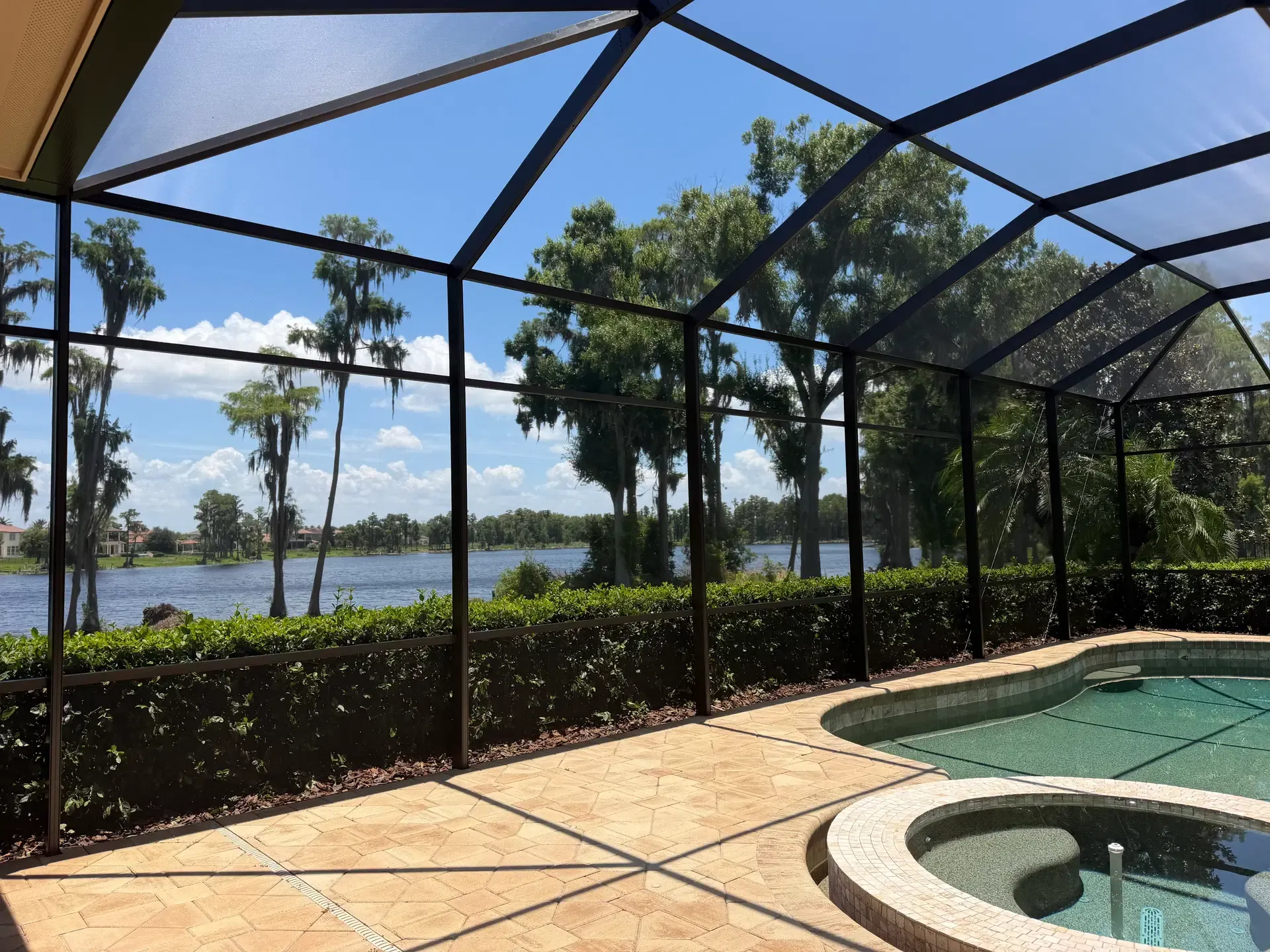A bright pool enclosure with clear screen panels and a view toward greenery and water