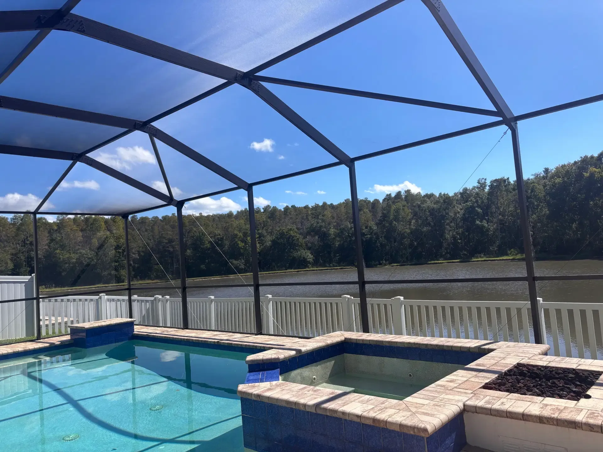 Pool enclosure with dark aluminum frame, swimming pool, and a view toward the lake.