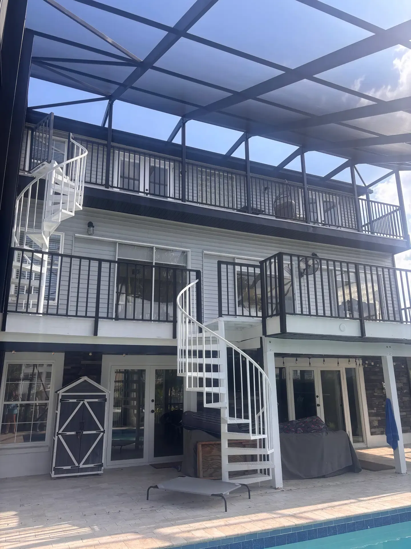 Two-story screened porch enclosure with dark aluminum framing and a spiral staircase beside the pool.